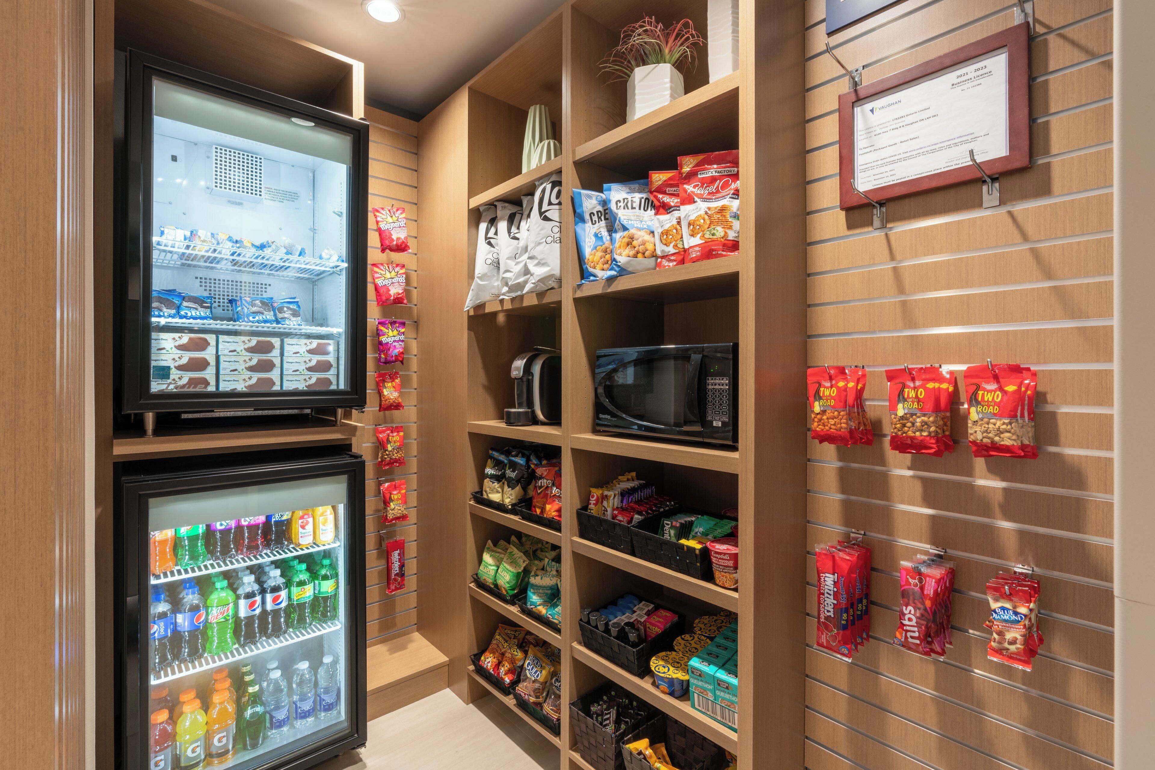 A snack and beverage display area with a microwave, vending machines, and a variety of snacks and drinks.