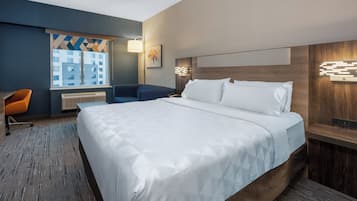 Et hotelværelse med en stor seng, et skrivebord, en stol og et vindue med udsigt til bygninger.