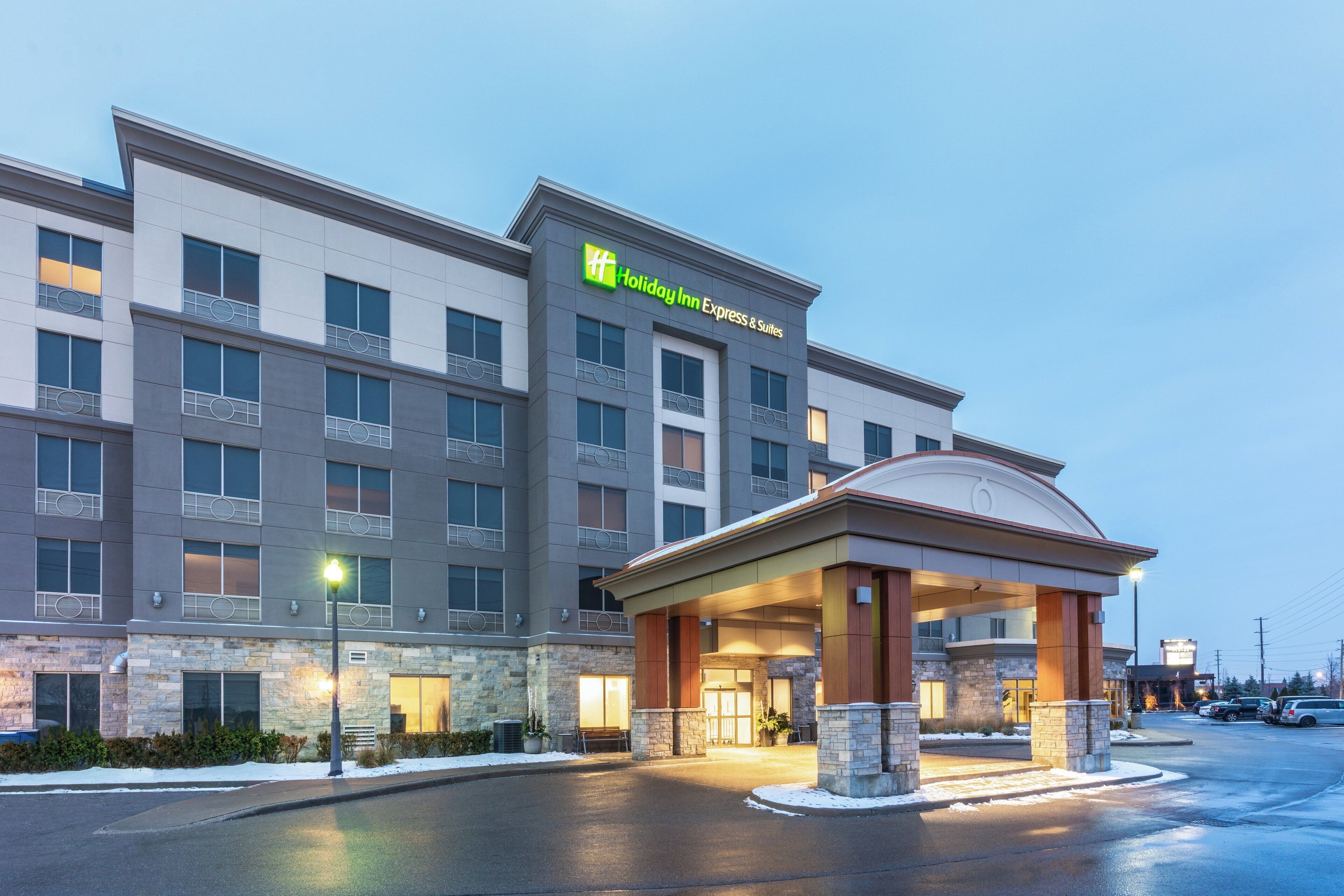 Ein Holiday Inn Express & Suites Gebäude mit modernem Design, inklusive überdachter Zufahrt und Parkplatz.
