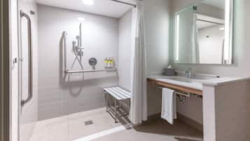 A modern bathroom with a shower, toilet, and sink, equipped with grab bars and a bench.