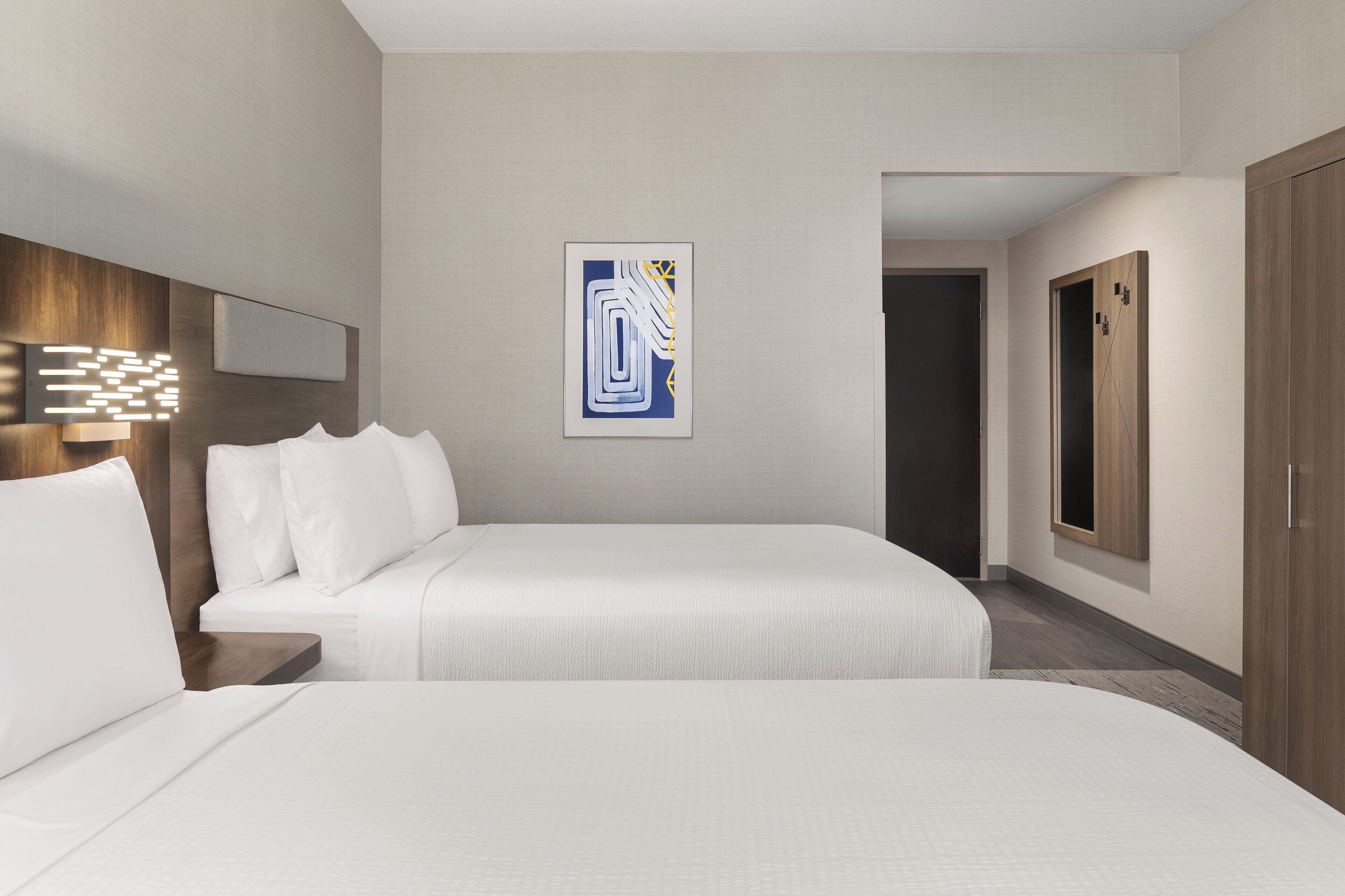 A hotel room with two beds, a wall-mounted artwork, a wooden headboard, and a wardrobe.