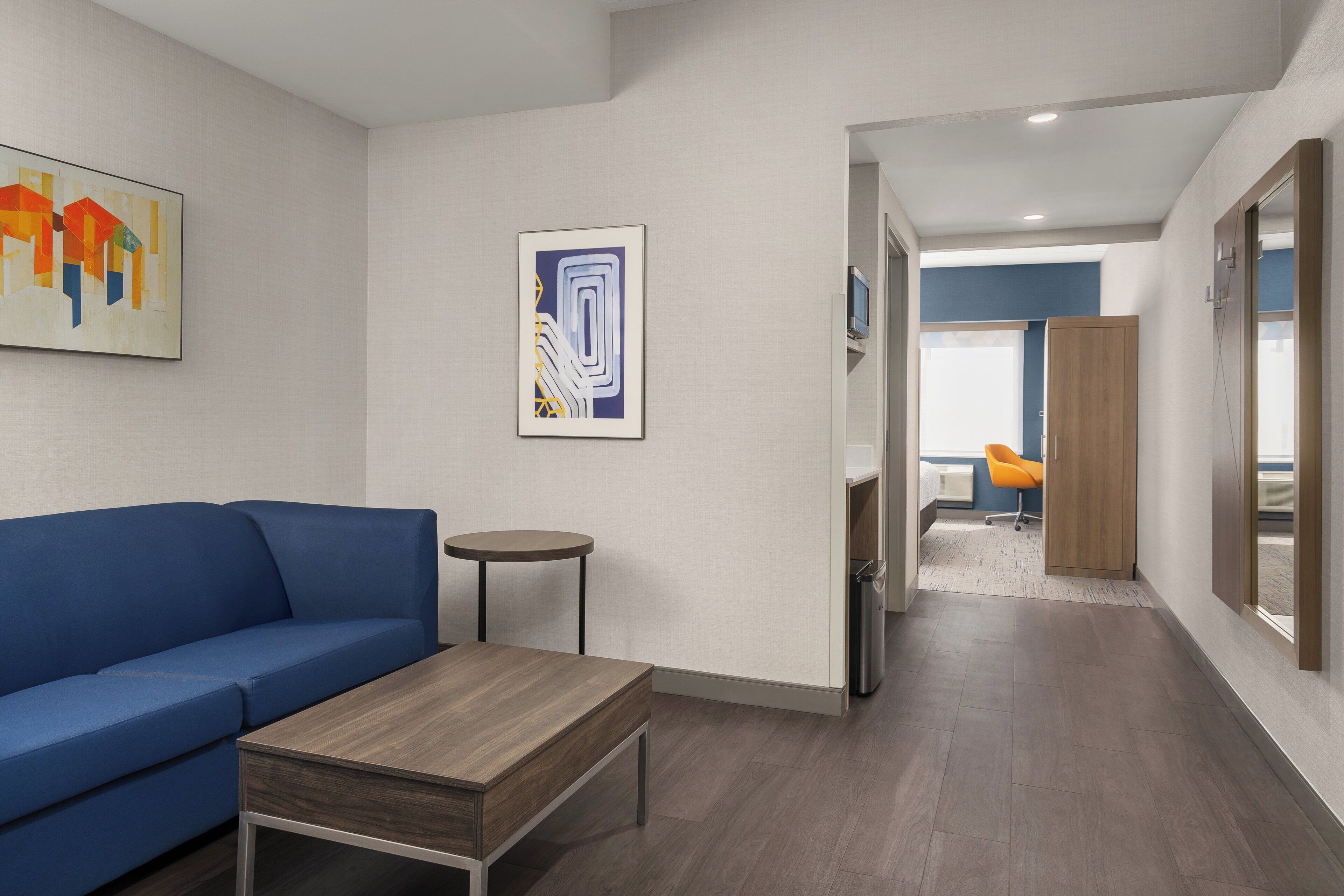 A modern hotel room with a blue sofa, a small round table, and a wooden coffee table.
