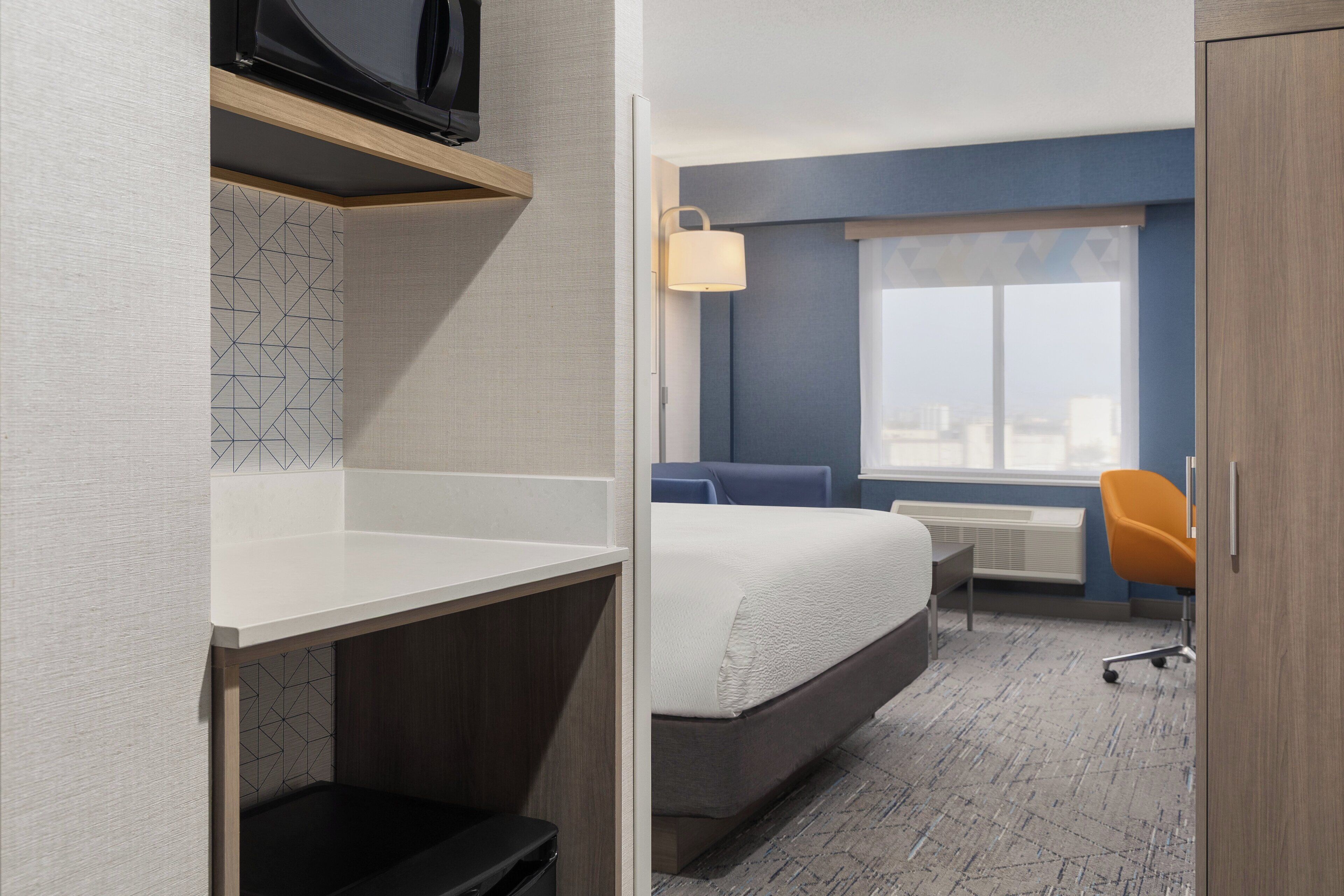 Une chambre d’hôtel avec un lit, un bureau, une chaise, une fenêtre et une vue sur la ville.
