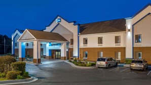 Un hotel con entrada central, varios espacios de estacionamiento y fachada bien iluminada.