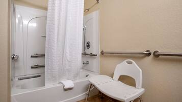 A bathroom with a bathtub, a shower, a white chair, and grab bars.