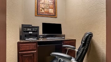 Escritório de canto com secretária, máquina de café, monitor e poltrona de couro.