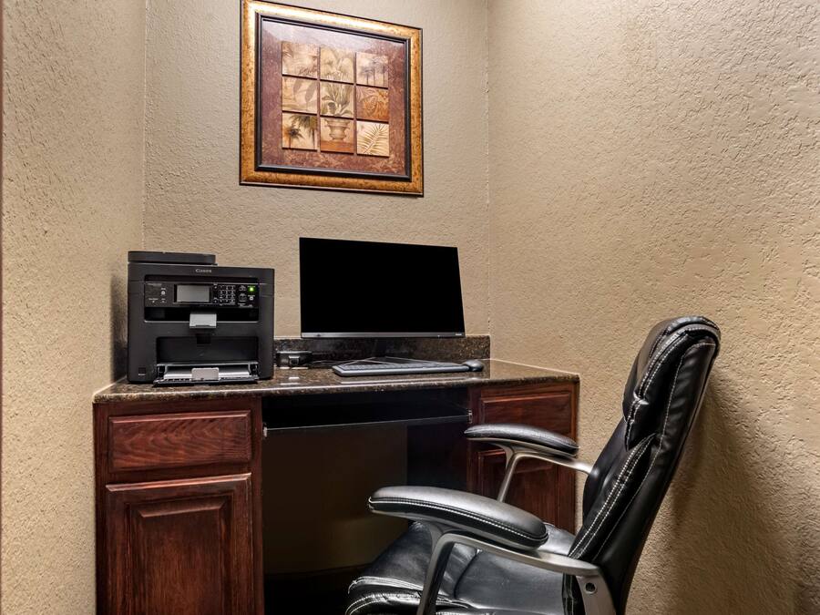 A corner office with a desk, a coffee maker, a monitor, and a leather chair.