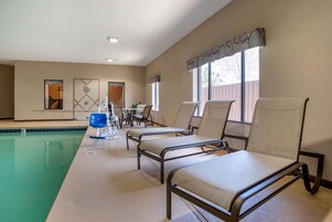 Zona de piscina con sillas de descanso, una mesa y una silla azul.