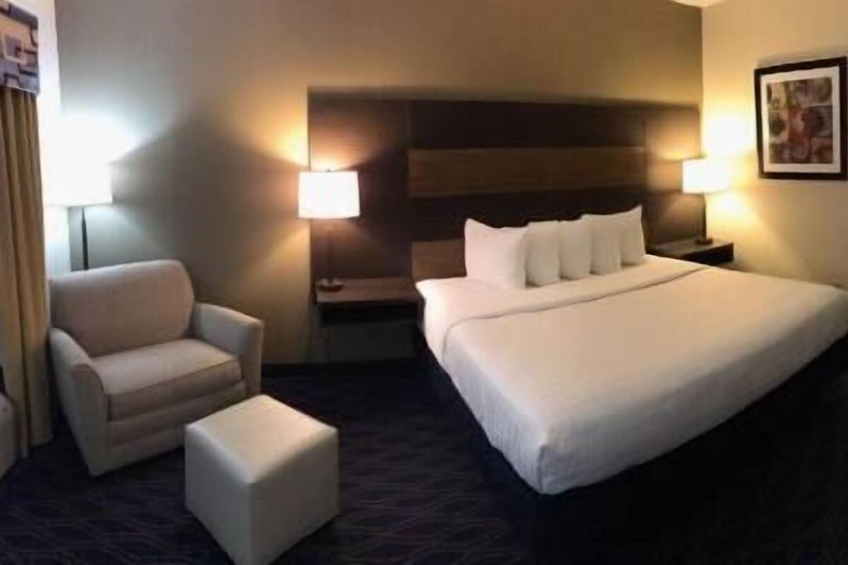 Quarto de hotel com uma cama grande, uma cadeira, uma mesa de cabeceira e um abajur.