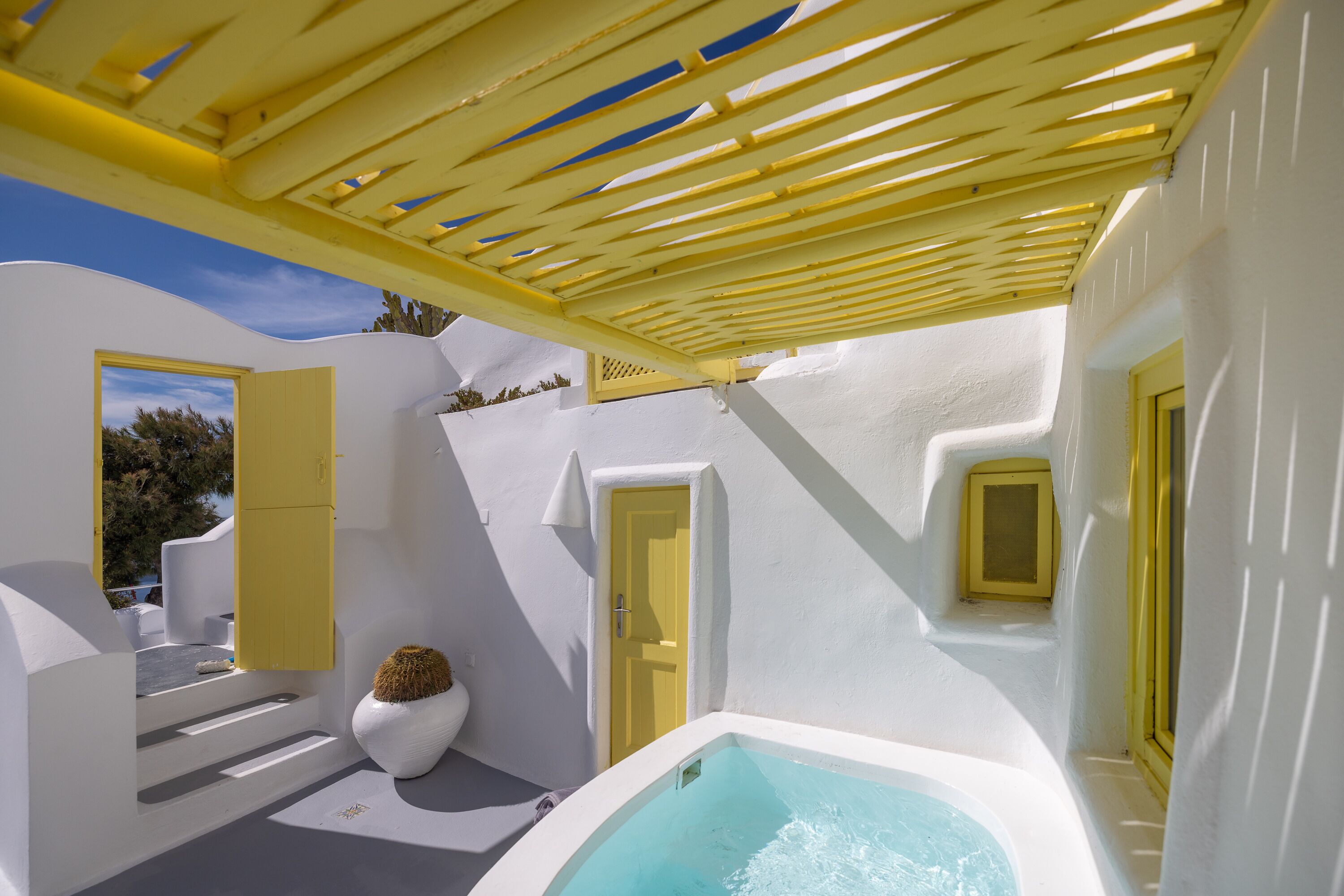 A white and yellow outdoor bathroom with a bathtub, a small white chair, and a door.