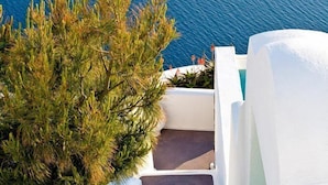 A white staircase leading down to a body of water, surrounded by white walls and greenery. - Dreams Luxury Suites (Santorini)