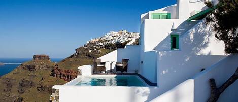 Un bâtiment blanc doté d’une piscine et d’un espace extérieur aménagé, offrant une vue sur un paysage côtier caractérisé par des bâtiments blancs et des falaises.