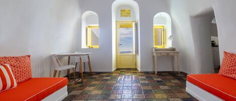 A room with a colorful tiled floor, a white sofa with orange cushions, a small table, and a chair.