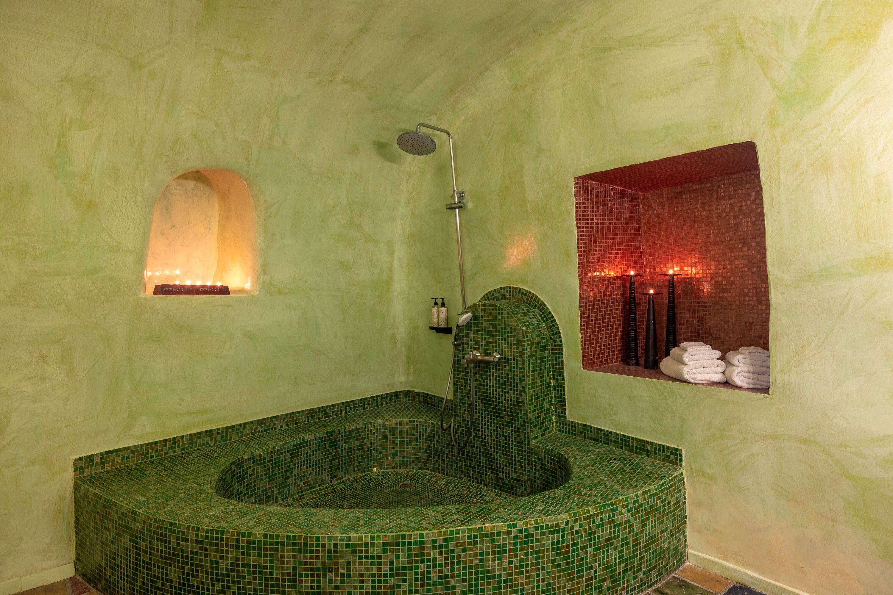 Eine Badewanne mit grünen Fliesen, eine kleine Nische mit einem Spiegel und ein Handtuchhalter mit Handtüchern.
