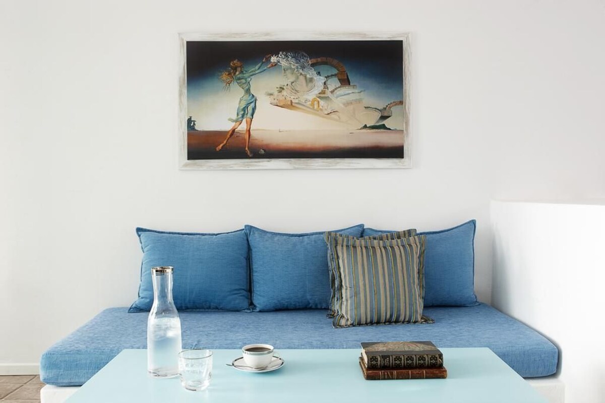 Quarto com um sofá azul, uma mesa de centro azul clara, uma obra de arte emoldurada e uma garrafa de água.