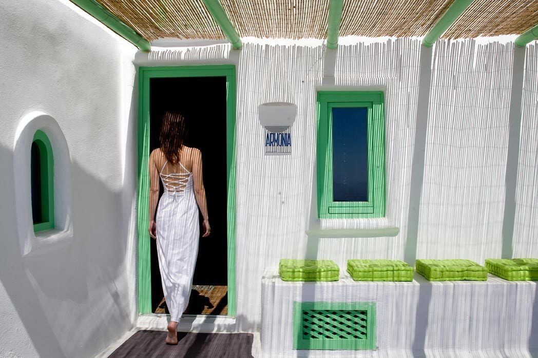 Une personne sort d’un bâtiment blanc agrémenté de touches de vert, notamment une porte, une fenêtre et un petit espace avec un banc.