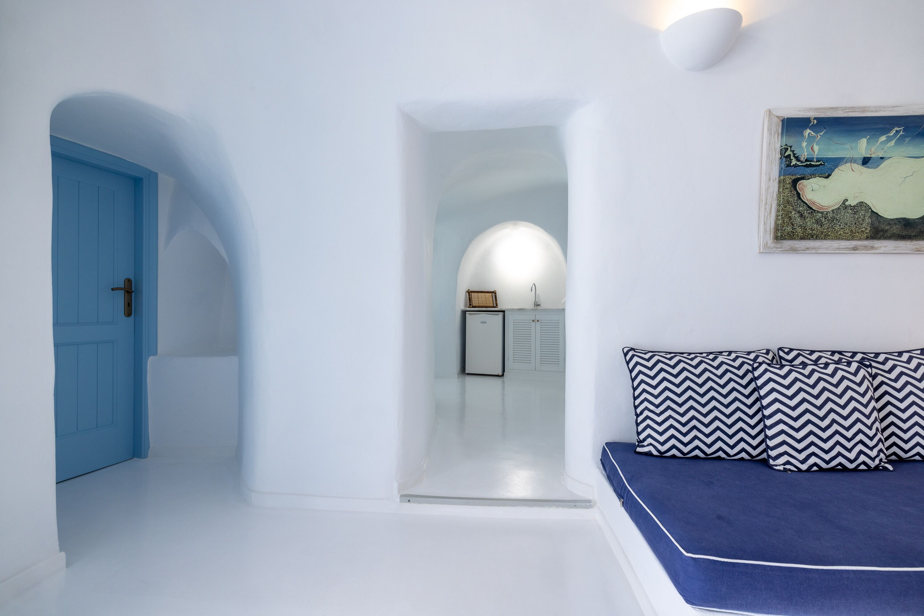 A room with a blue door, a bed with patterned pillows, and a painting on the wall.