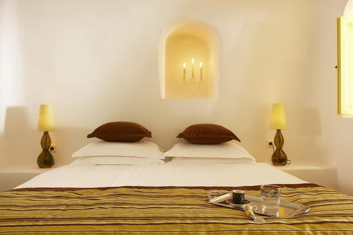 A hotel room with a bed, two lamps, a tray with a cup and glass, and a wall-mounted candle holder.