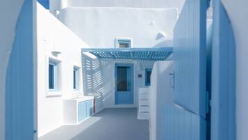 A narrow, white-walled corridor with a blue door at the end, leading to a room with a blue ceiling and a white ceiling fan.