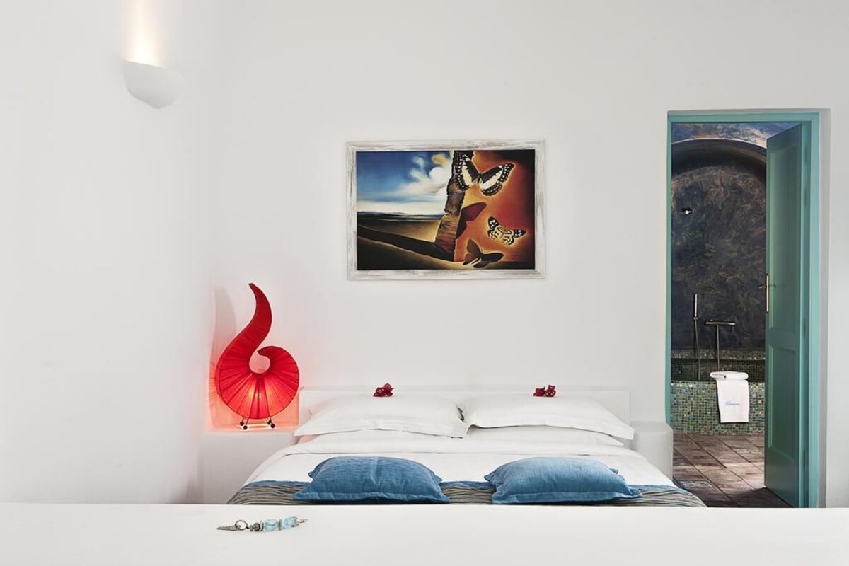 A bedroom with a bed, pillows, a red sculpture, and a framed picture on the wall.