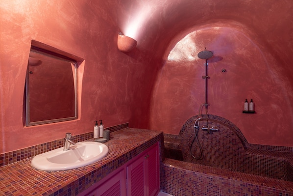 A bathroom with a pink tiled wall, a sink, a mirror, and a shower. - Dreams Luxury Suites (Santorini)