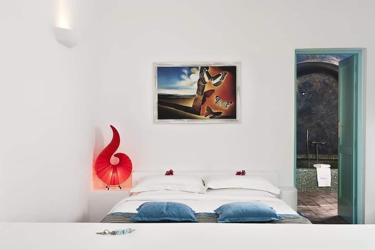 A bedroom with a bed, pillows, a red sculpture, and a framed picture on the wall.