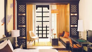 A hotel room with a bed, a sofa, a desk, a chair, a TV, and a window with curtains.