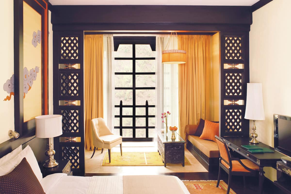 Habitación de hotel con cama, sofá, escritorio, silla, televisor y ventana con cortinas.