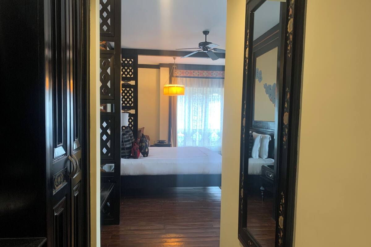 Una habitación de hotel con cama, ventilador de techo y mesita de noche con lámpara.
