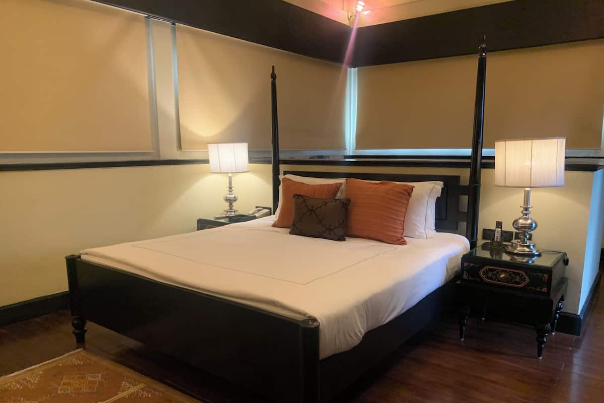 Una cama con dosel, ropa de cama blanca, dos mesitas de noche con lámparas y una alfombra estampada.