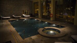 An indoor swimming pool with lounge chairs and a hot tub.