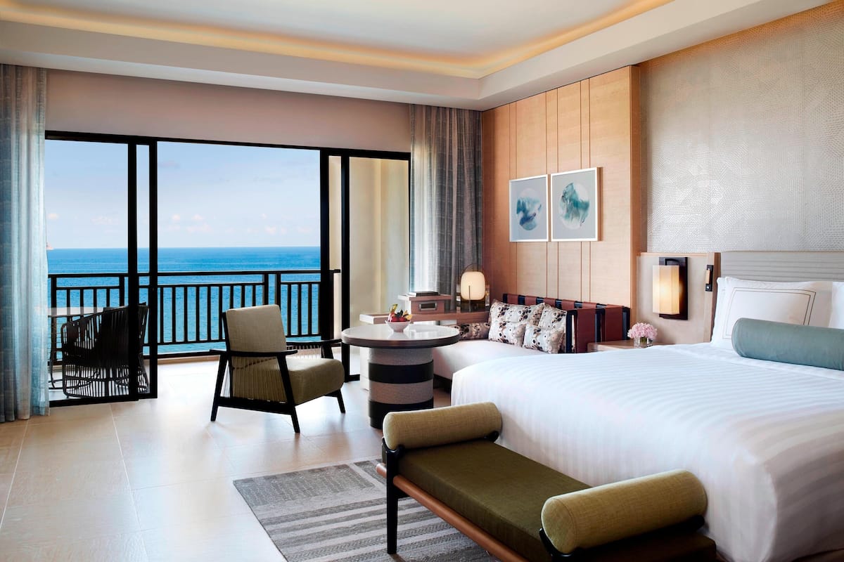 A hotel room with a large bed, a desk, a chair, and a view of the ocean.