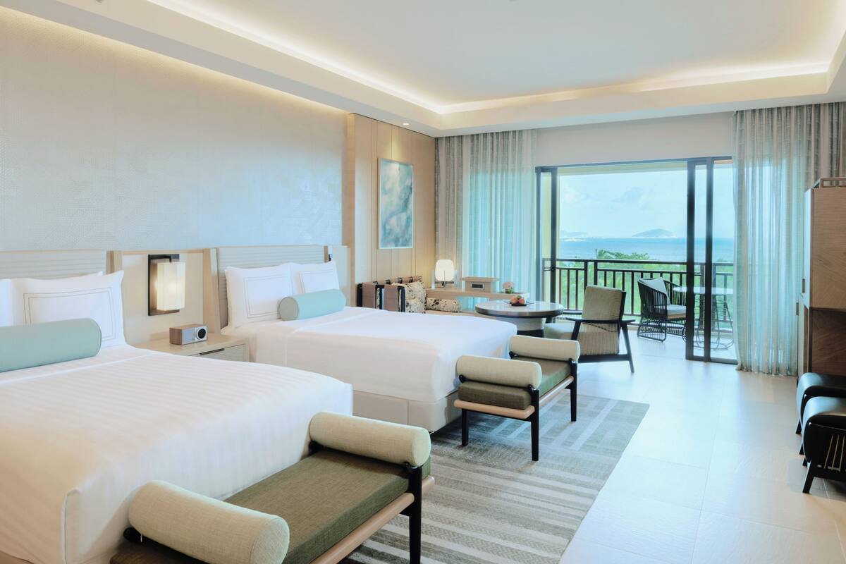 A hotel room with two beds, a sitting area with chairs, a small table, and a balcony with a view.