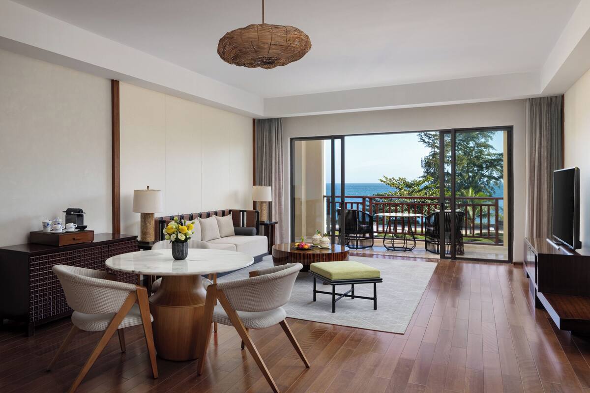 A modern hotel room with a large balcony, a round dining table, and a sofa.