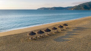 A beach with a row of sun loungers and umbrellas, a clear sky, and a calm sea.