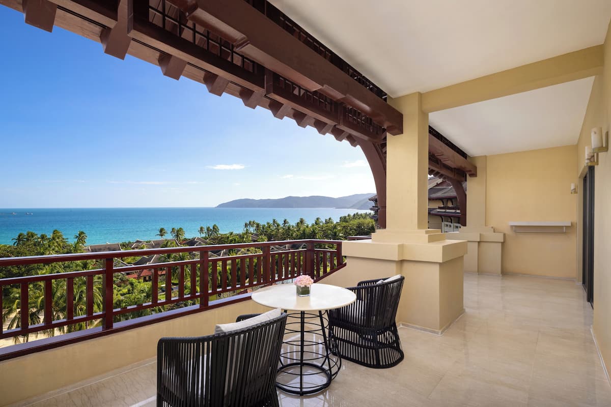 A balcony with a view of the ocean, a round table with chairs, and a small flower vase.