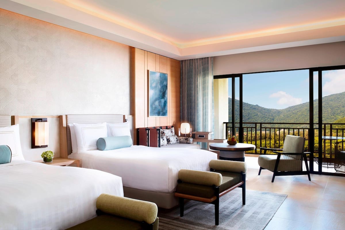 A hotel room with two beds, a sitting area with chairs, a small table, and a large window offering a mountain view.