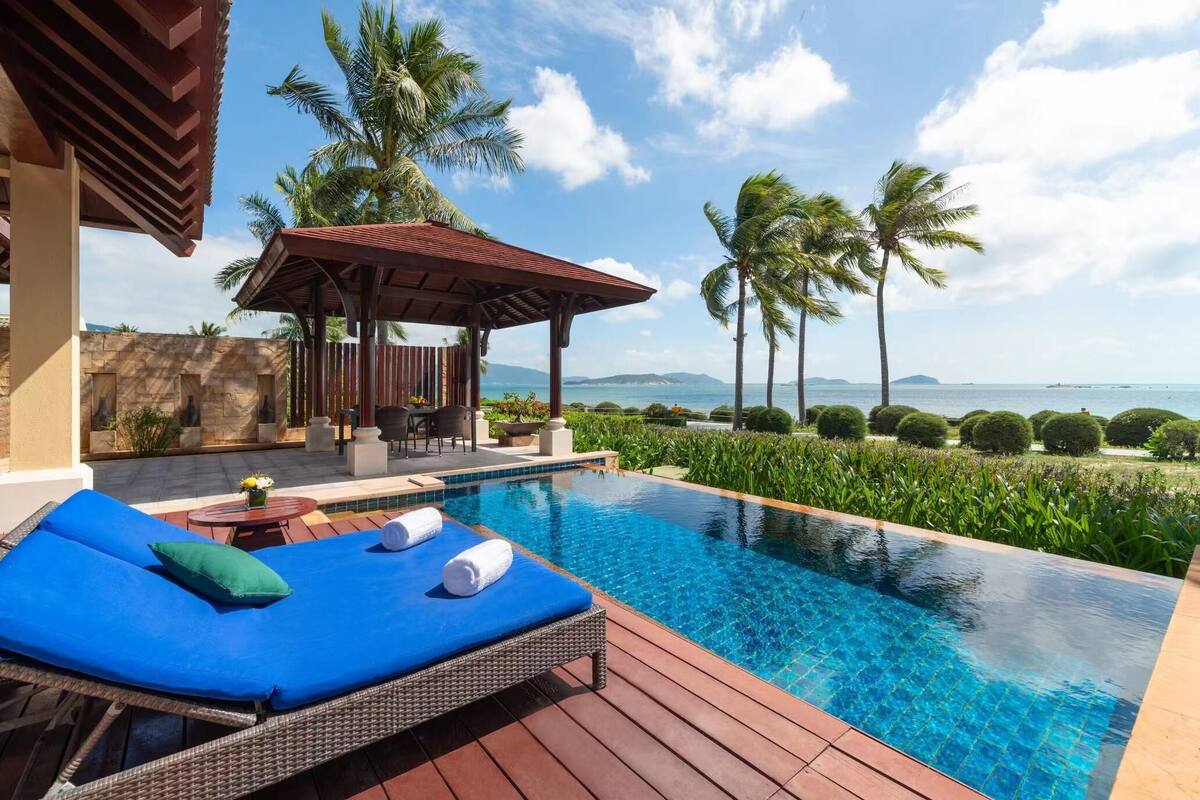 A poolside area with a lounge chair, a small table with a vase, and a pergola.