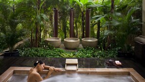 Un espace de bien-être avec un jacuzzi entouré d’une végétation luxuriante et de piliers en pierre.