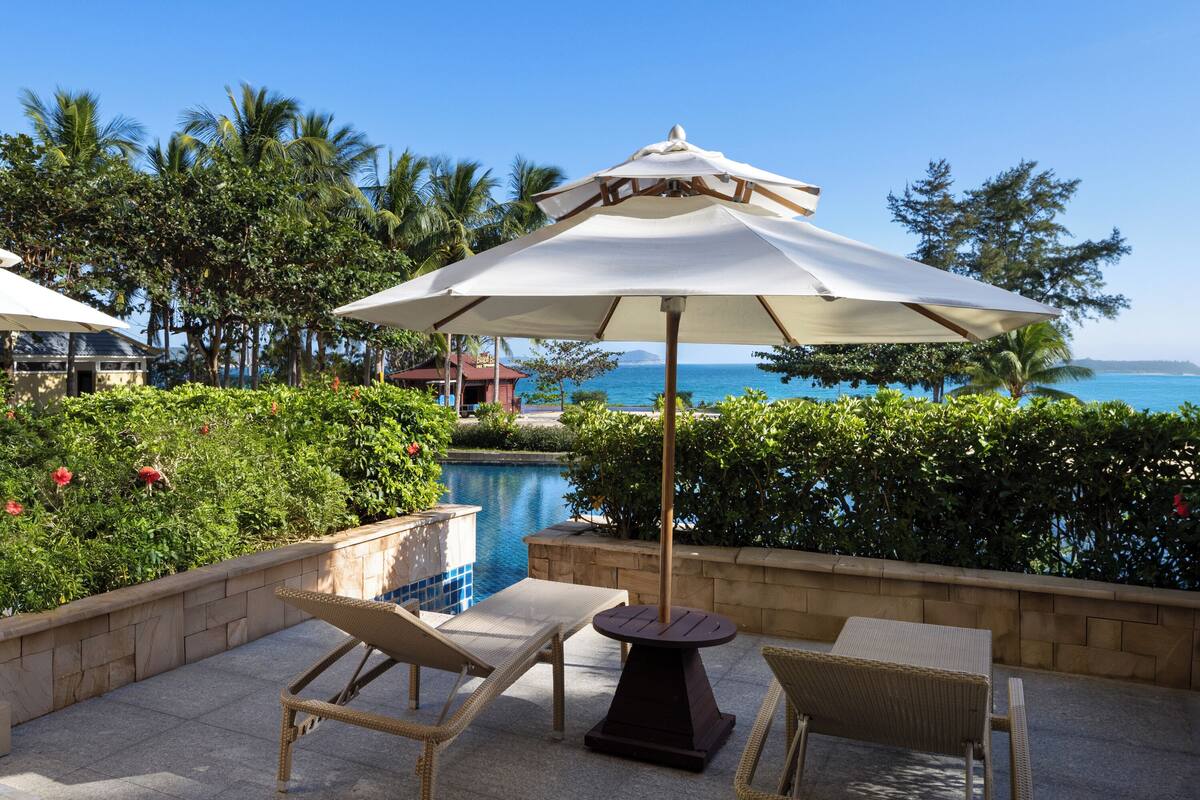 A poolside area with lounge chairs and an umbrella, overlooking a pool and the ocean.