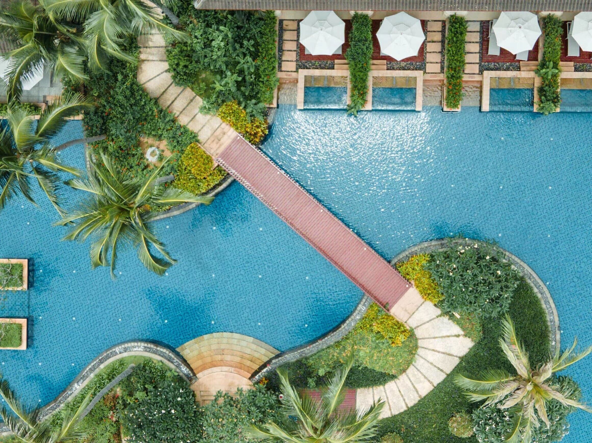 Vista aérea de un resort con una piscina central, rodeado de exuberante vegetación y palmeras.