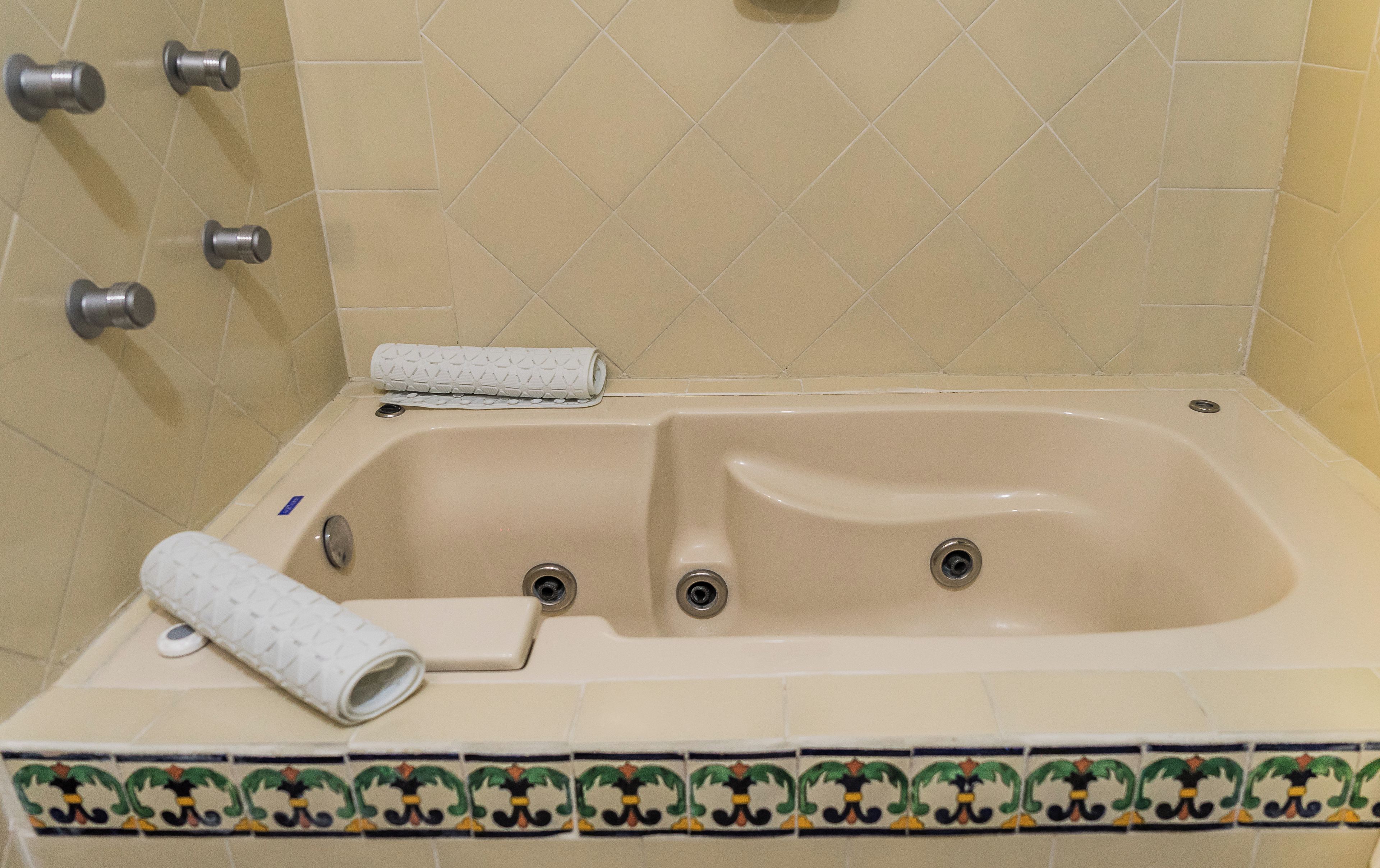 A bathtub with two faucets, a rolled-up towel, and a drain.