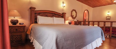 Un dormitorio con una cama grande, cabecera de madera y techo de madera. Hay apliques y un espejo en la pared.