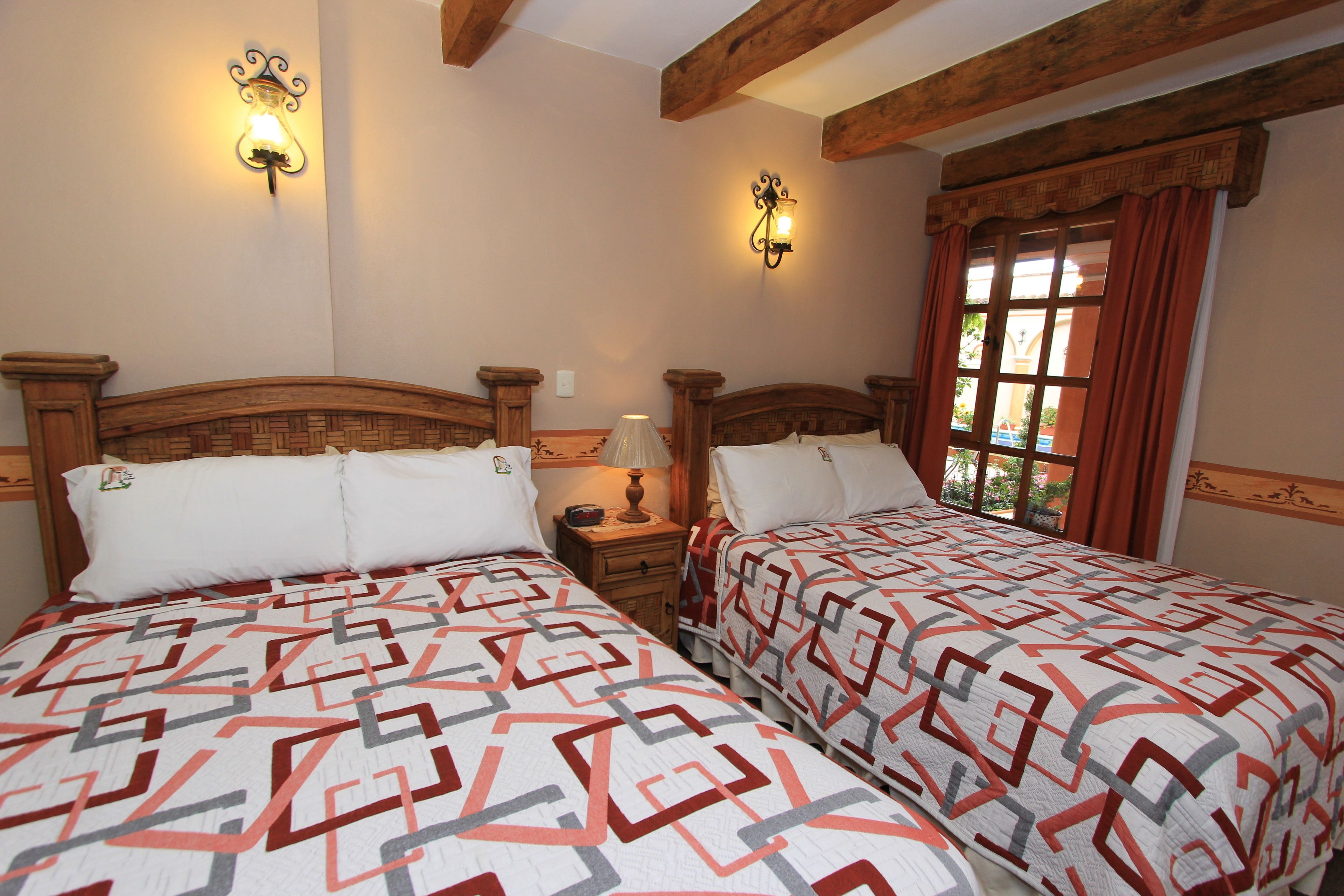 Ein Zimmer mit zwei Betten, jedes mit einer gemusterten Tagesdecke, Holzkopfteilen und Wandleuchten.