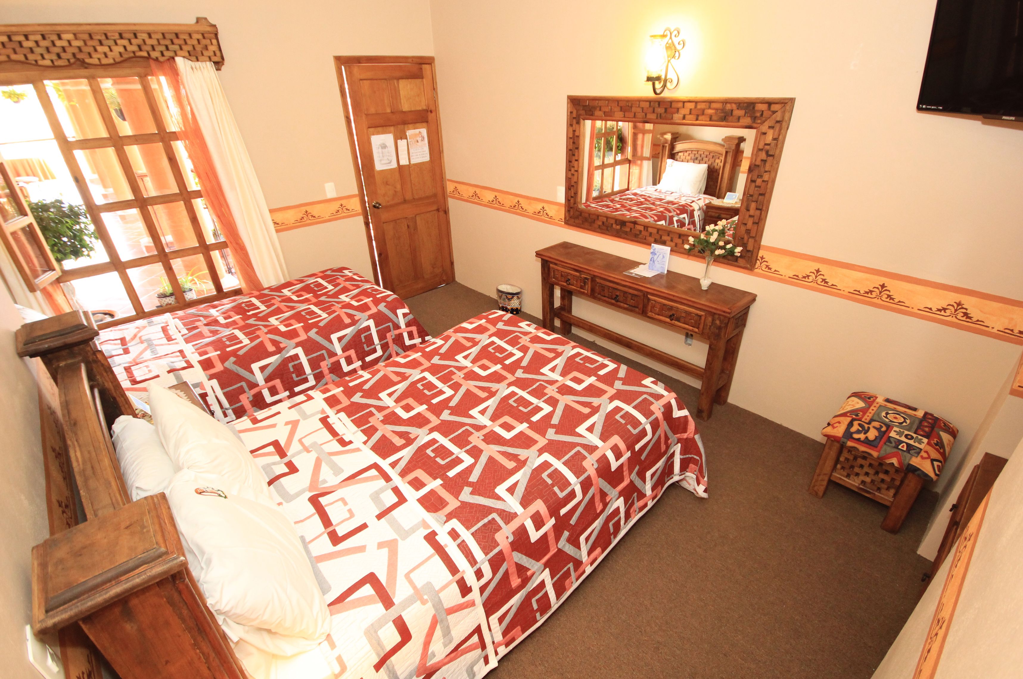 A bedroom with a large bed, a wooden dresser, a mirror, and a small table with a lamp.