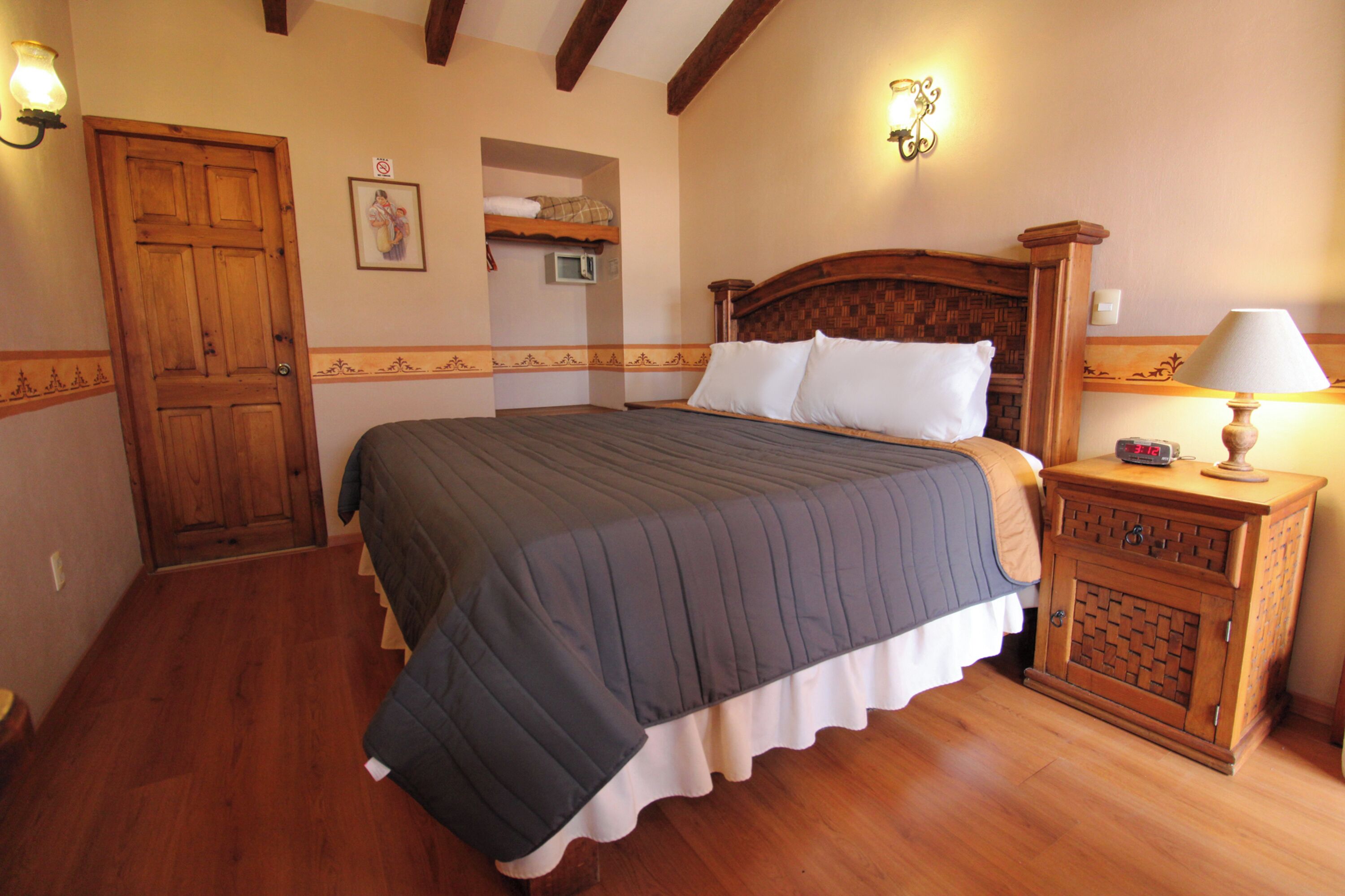A bedroom with a wooden bed, a nightstand with a lamp, a wooden wardrobe, and a door with a light fixture.