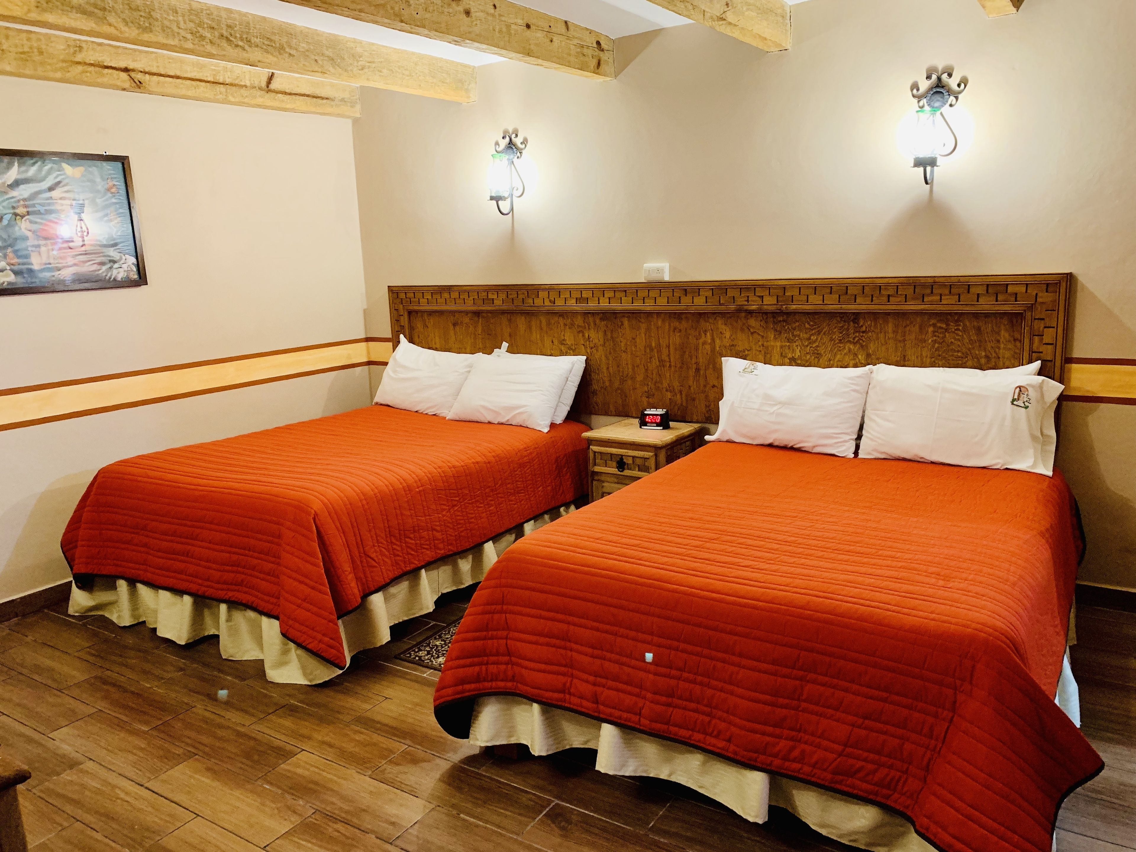 A hotel room with two beds, wooden headboards, a nightstand with a clock, and a painting on the wall.