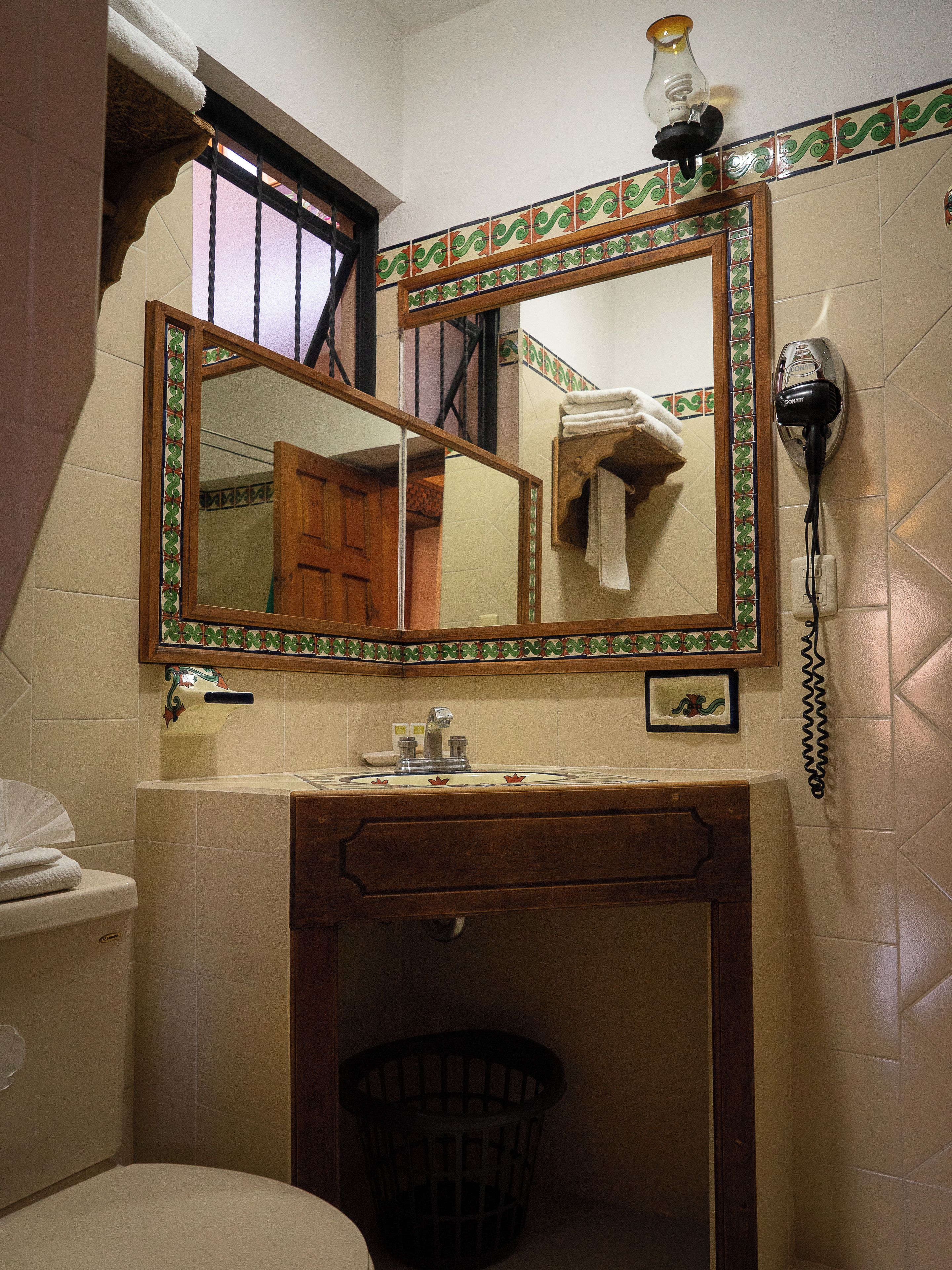 A bathroom with a mirror, a hairdryer, a towel rack, and a waste basket.