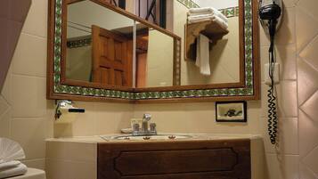 A bathroom with a mirror, a hairdryer, a towel rack, and a waste basket.