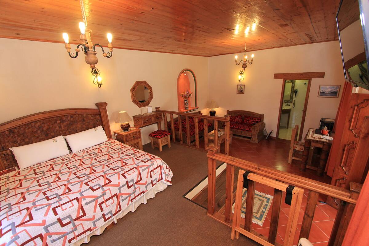A bedroom with a large bed, wooden ceiling, and a small table with a lamp.